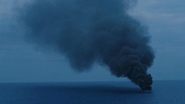Image from Europe's New Faces review showing a burning ship at sea with a large plume of black smoke rising.