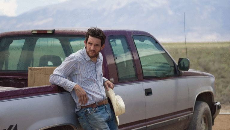 Rebuilding film review: Man leans against truck in Max Walker-Silverman's film, holding a cowboy hat, mountains in background.