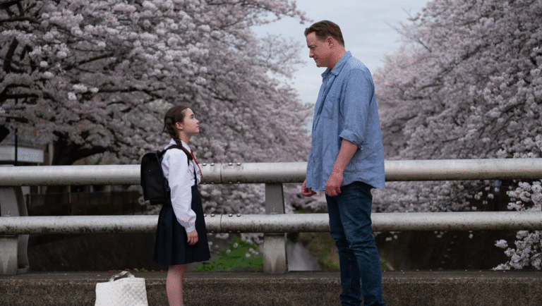 Rental Family movie scene: A young Japanese schoolgirl and an American man stand near cherry blossom trees.