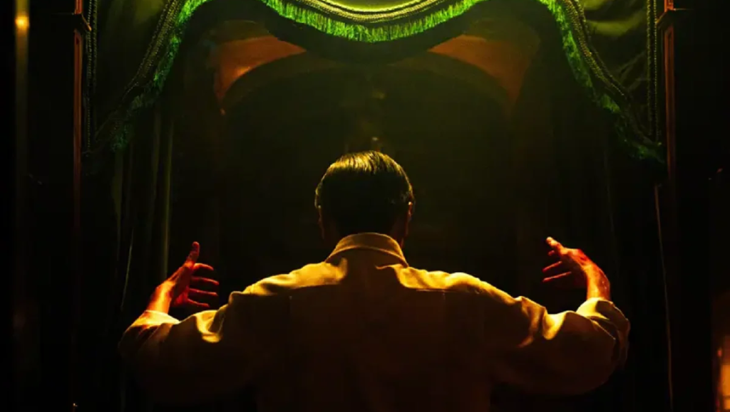 Bi Gan's Resurrection film scene: Man stands before a stage with green curtains, arms outstretched in pursuit of autonomy.