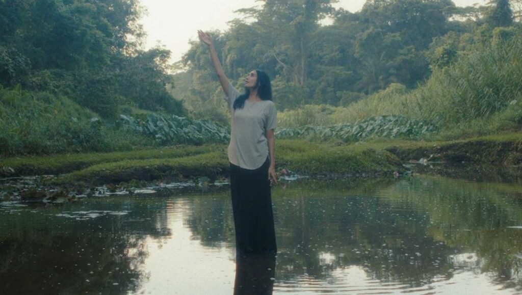 Film still from "We Learned to Breathe" at Singapore International Film Festival 2025; woman stands in water, arm raised.