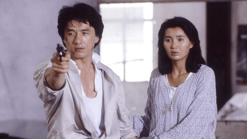 Police Story film still: Jackie Chan points a gun, with a woman standing beside him. Action movie scene.