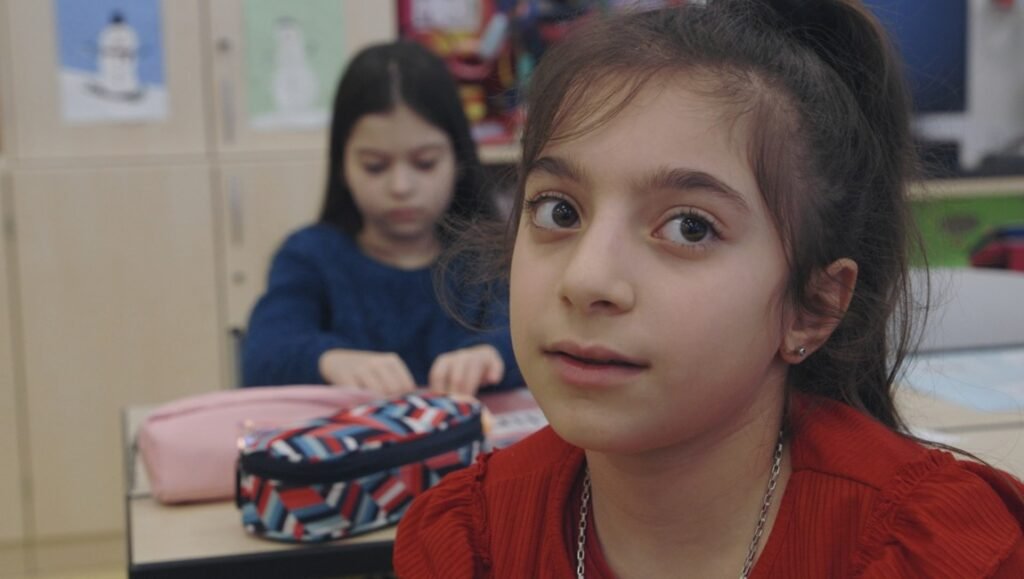 Austrian schoolgirls in classroom. Focus on girl in the foreground wearing red, with another girl blurred in the background.