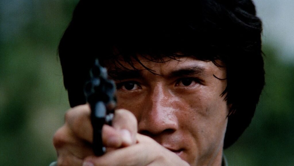 Jackie Chan in Police Story, holding a gun. Action movie scene of Chan aiming a pistol with intense focus.