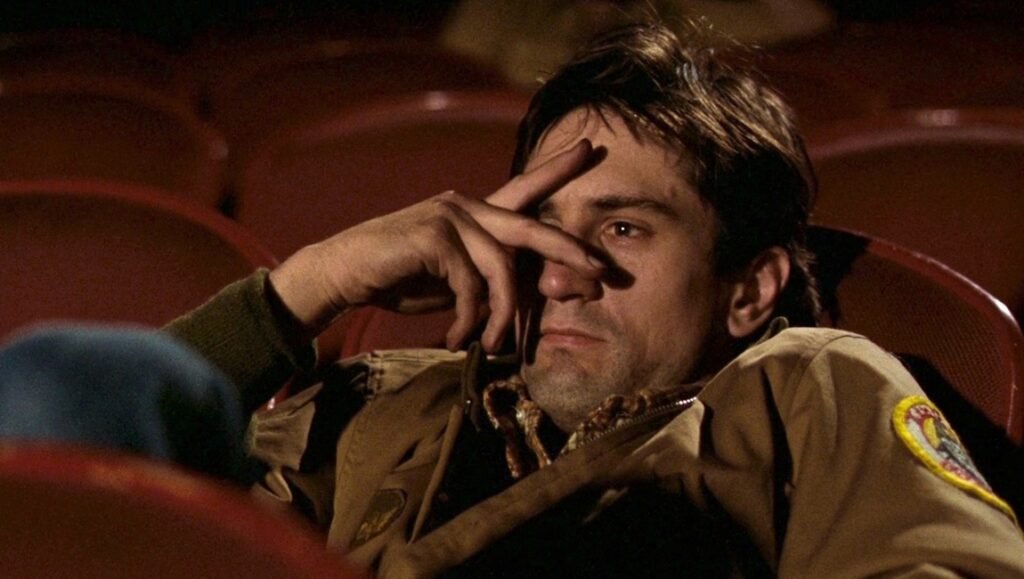 Robert De Niro in Taxi Driver (1976) looking distressed in a theater seat, Columbia Pictures film still.
