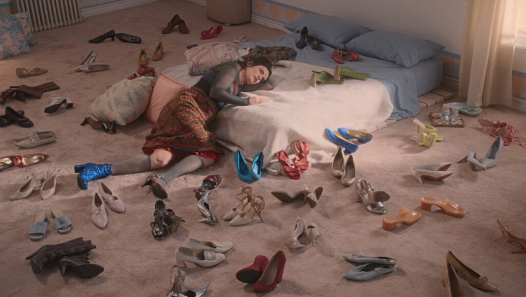 Amanda Kramer film still: Woman lies on bed surrounded by many shoes on the floor. 'By Design' movie scene.
