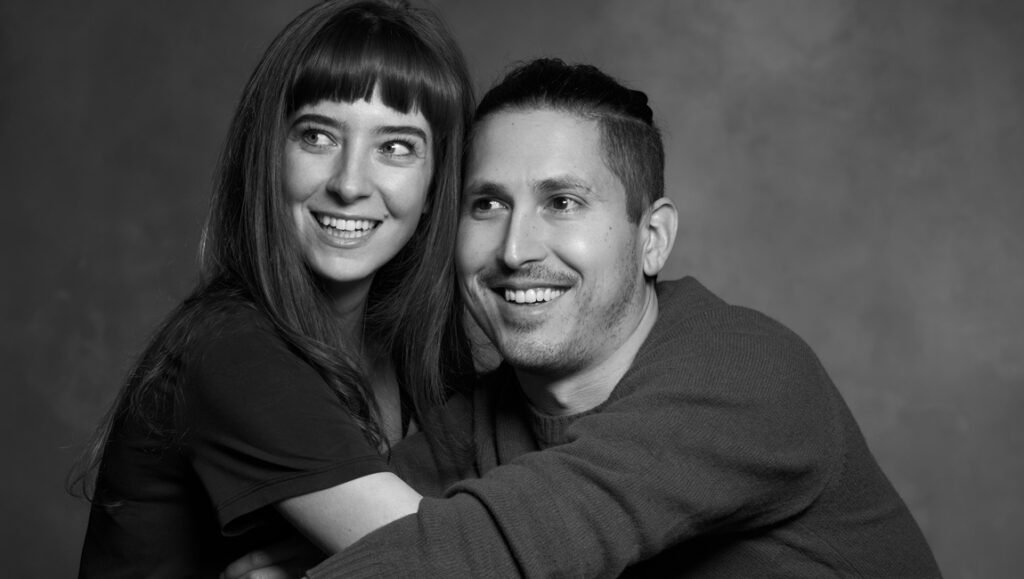 There’s No Perfect Relationship: Madeleine Sims-Fewer & Dusty Mancinelli on Honey Bunch Honey Bunch directors' headshot: Smiling woman with bangs and man in sweater in black and white. Film directors portrait.