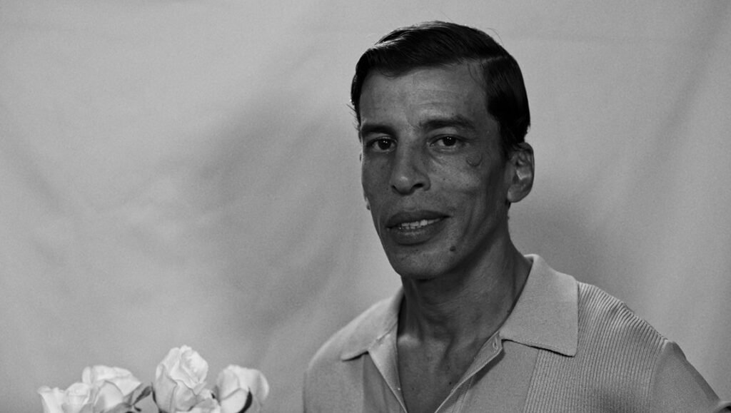 Black and white film still portrait of an Arab actor with roses, classic cinema aesthetic.