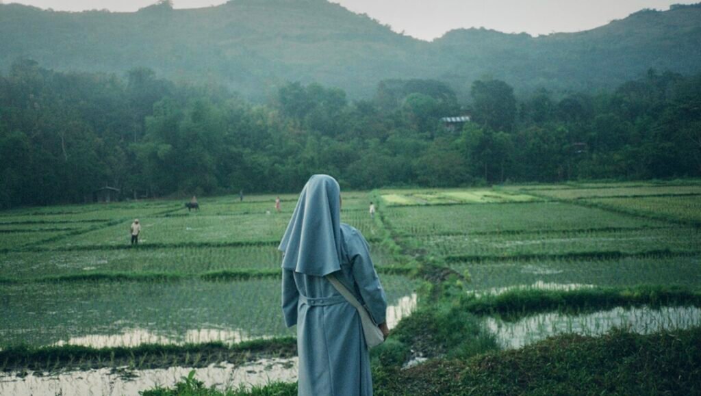 James J. Robinson's "Firstlight" film still: Nun gazing at rice fields, mountain backdrop. IFFR26 film festival image.