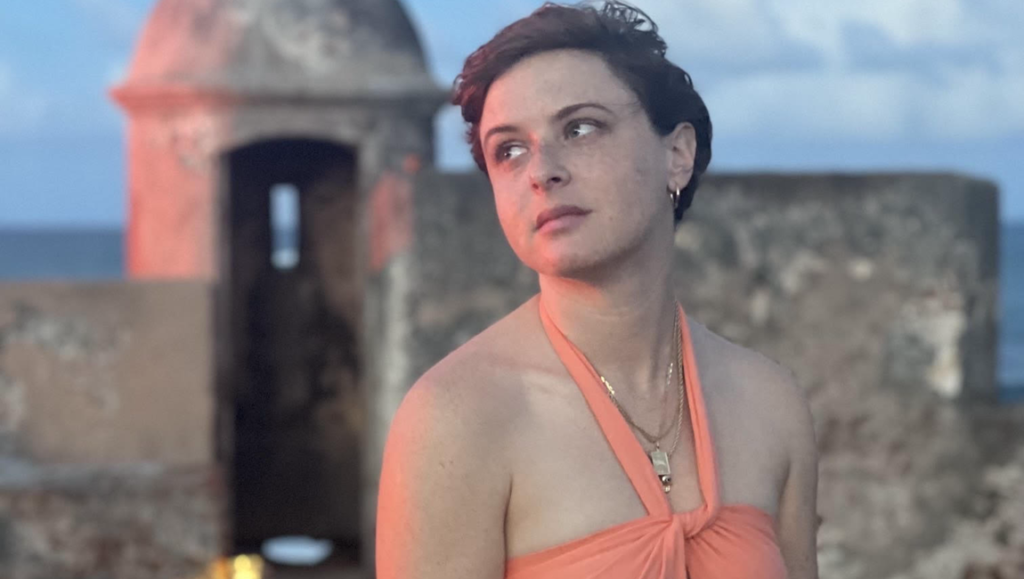 Faith, Art, & Community: A Conversation with Caroline Golum on Revelations of Divine Love Caroline Golum interview, portrait by Jessica Rionero. Author poses near historic Puerto Rican fort.