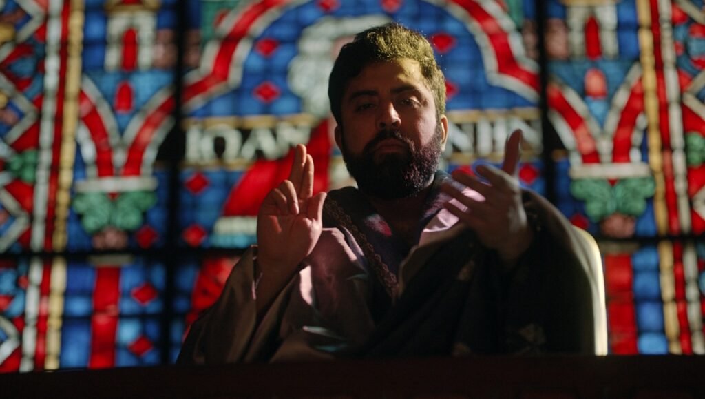 Caroline Golum Interview: Man with beard in front of stained glass, gesturing with hands.