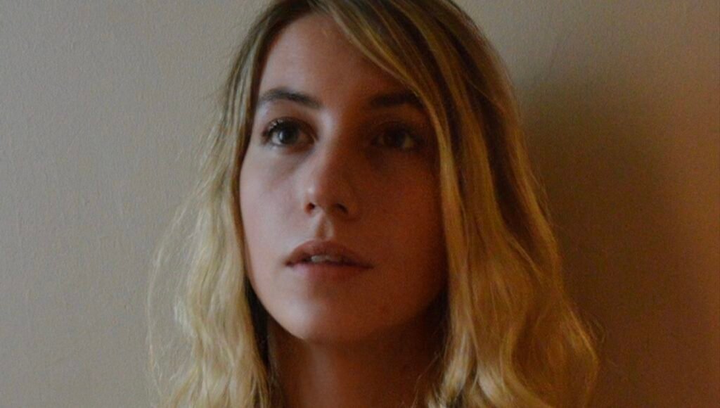 I Don’t Make Scary Movies: An Interview with Alice Maio Mackay Portrait of Amalia Stramatos, blonde woman looking up with wavy hair and neutral expression, headshot.