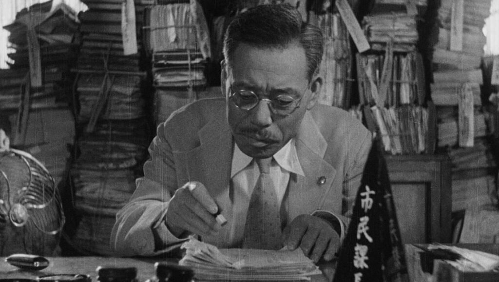 Akira Kurosawa's Ikiru: Kanji-marked flag, bureaucrat Kanji Watanabe stamps documents, surrounded by stacked papers, classic cinema.