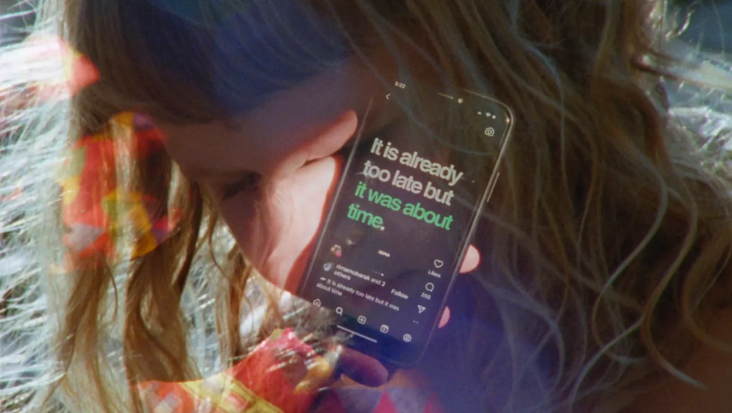 Cosmic Rays: Woman holding a phone with the text "It is already too late but it was about time" displayed.