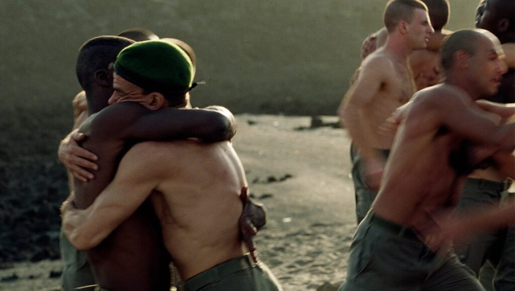 Beau Travail film still: shirtless soldiers wrestling and embracing on a beach, Criterion Collection edition.