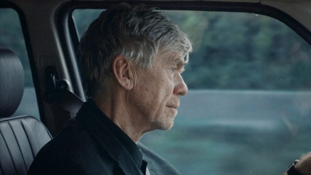 Cinéma du Réel film still: Older man driving in London, looking out the window. "In-I In Motion" film scene.