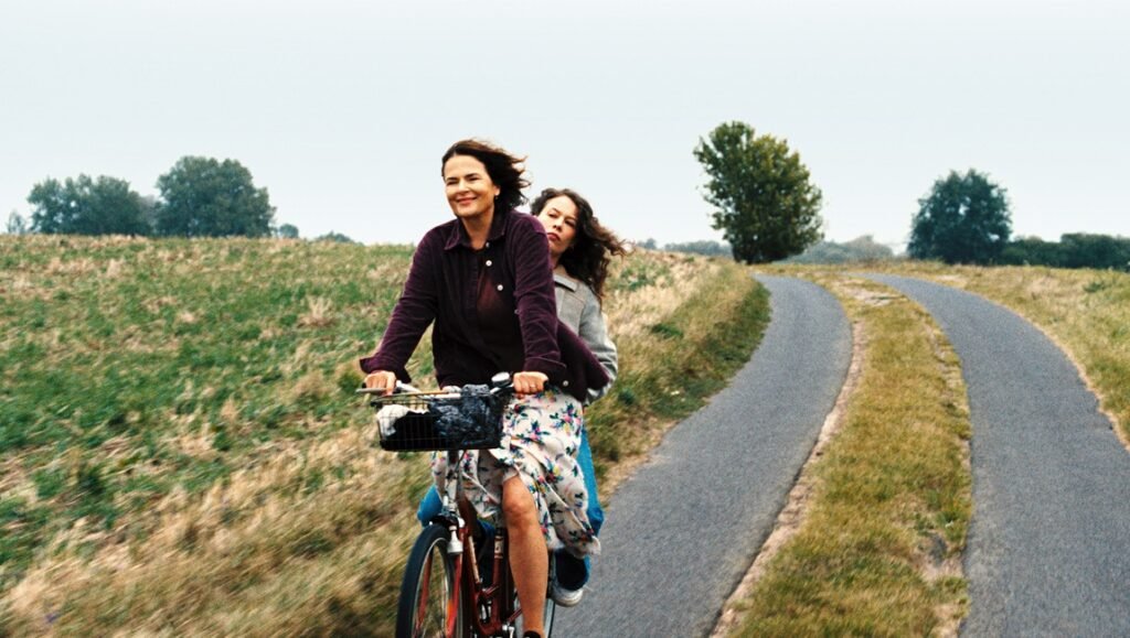 Two women enjoy a bike ride on a country road, promoting themes of freedom and connection in "A Borrowed Breath".