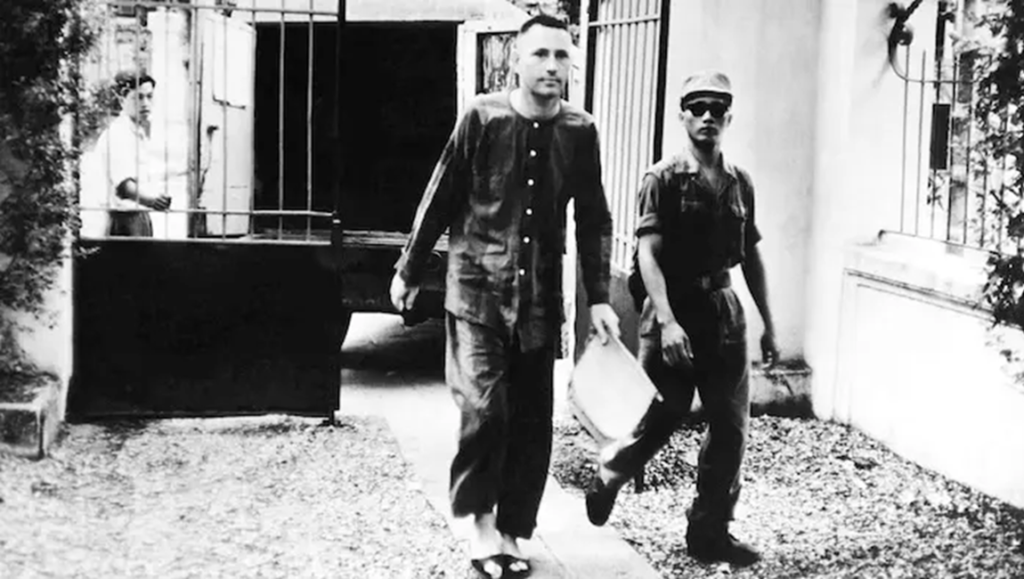 Pilots in Pajamas: Heynowski & Scheumann film still shows a captured pilot escorted by a guard, in black and white.