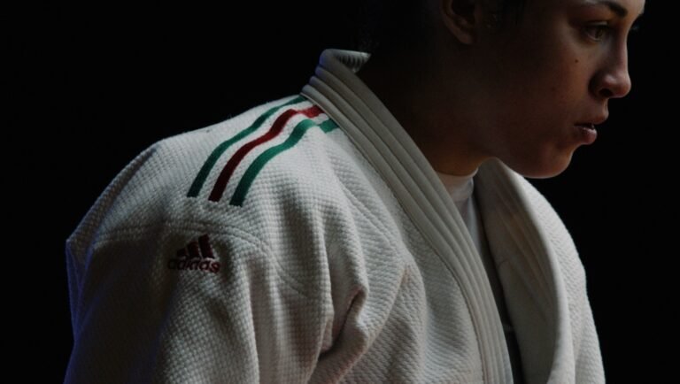 Close-up of a judoka athlete in Adidas gi, focused on competition, wearing a white uniform with green and red stripes.