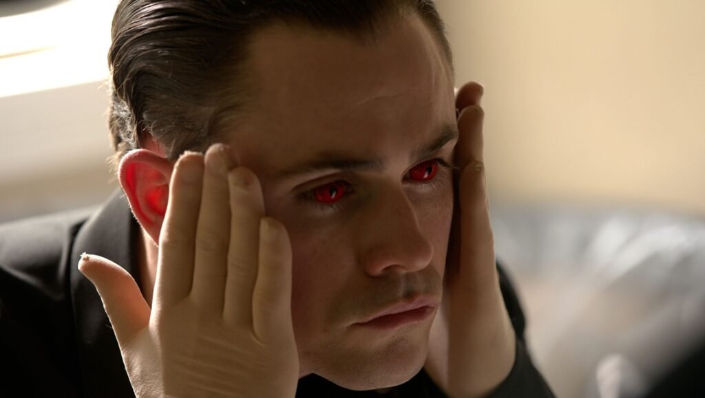 Close-up of a man with intense red eyes, hands near temples, hinting at horror for "Faces of Death" discussion.