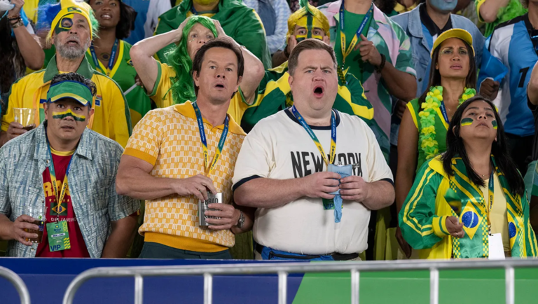 Balls Up movie scene: Mark Wahlberg and fellow fans react at a sports event, wearing team colors and lanyards.