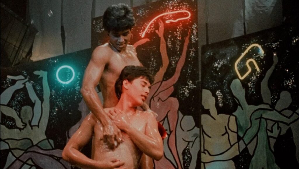 Kani-Macho-Dancer5.jpg: Two shirtless dancers in LAFM 2026, illuminated by neon lights, showcasing human intimacy feats.