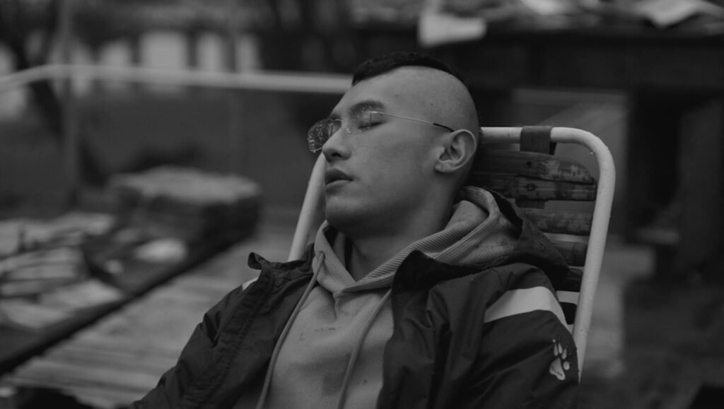 Man with glasses relaxing in chair in black and white.