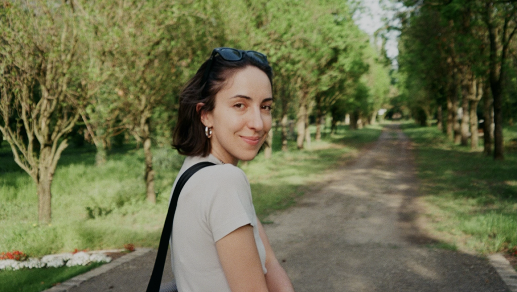 Just Because It’s Personal, That Doesn’t Make It Easy: Sophy Romvari on Blue Heron Sophy Romvari interview image: Young woman smiling in a park, Muri Darida in background, casual style, sunglasses on head.