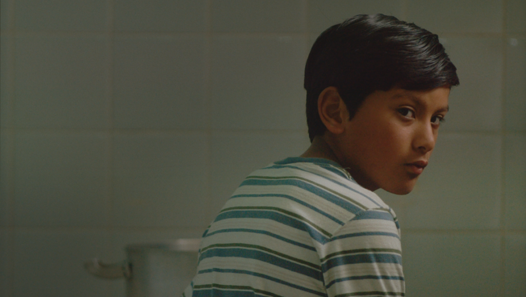 A young boy in "The River Train" film, looking back with a serious expression. Indie film review, coming-of-age drama.