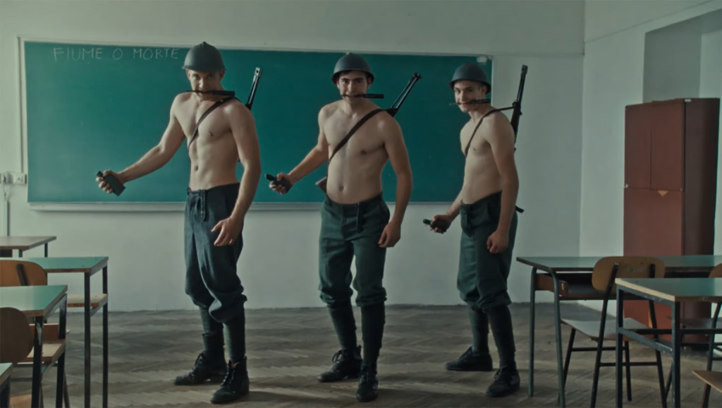 Fiume o Morte essay image: Three shirtless soldiers in a classroom holding weapons, conveying historical essay themes.