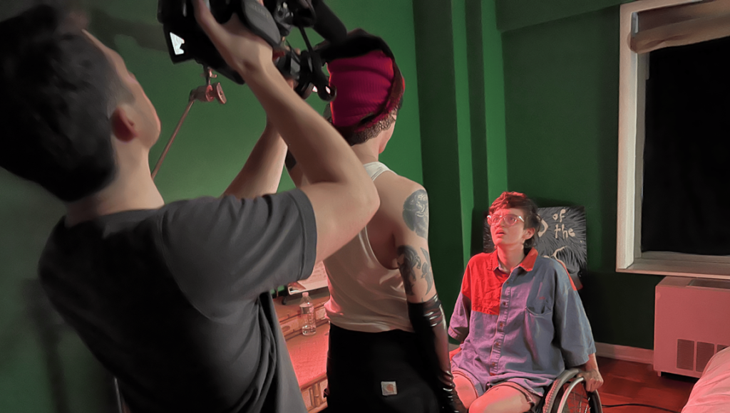 Josh Heaps filming a scene with a person in a wheelchair and another wearing a red hat in front of a green screen.