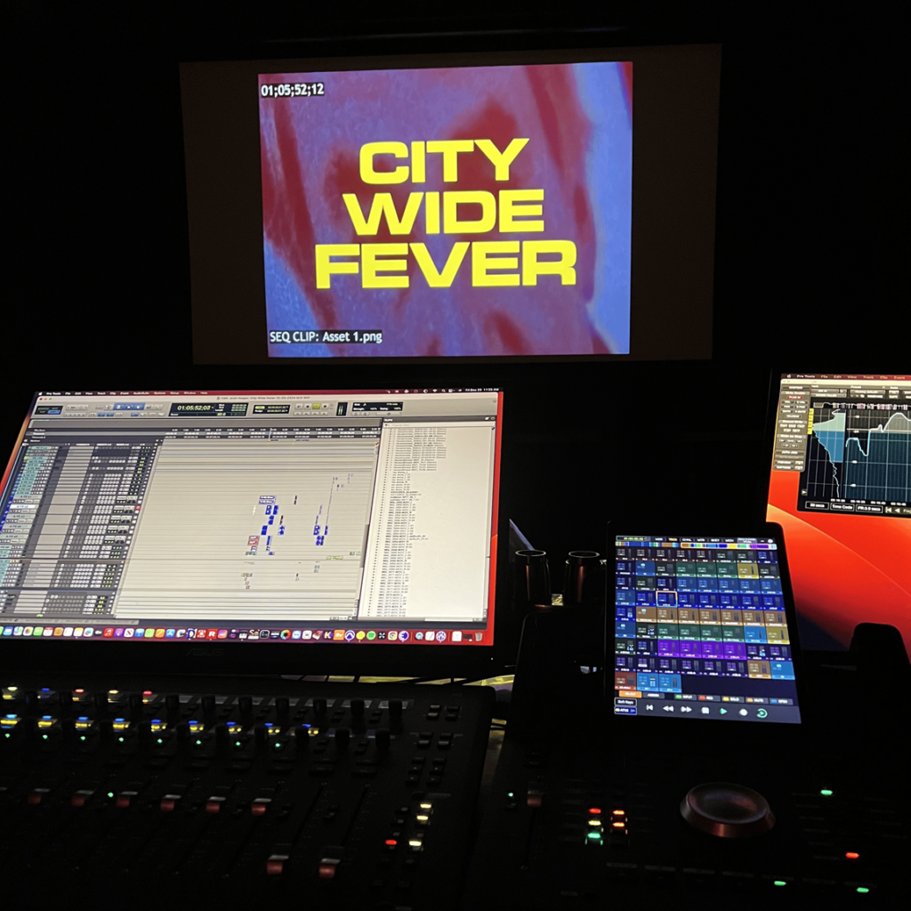 Josh Heaps working on "City Wide Fever", showing audio mixing desk, timeline and visual display in dark studio.