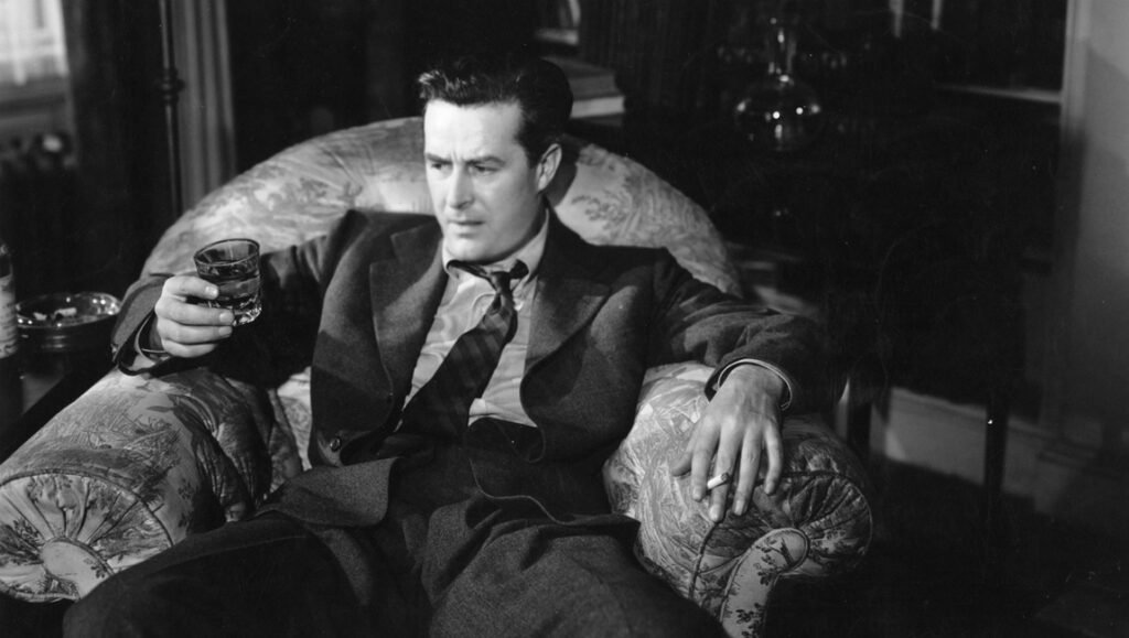 Ray Milland in 'The Lost Weekend' reclines in an armchair, holding a glass with liquid in one hand and a cigarette in the other.