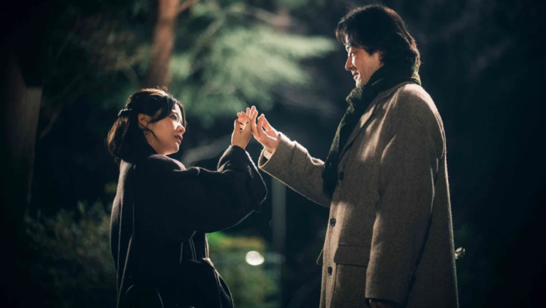 A woman and a man face each other, their hands nearly touching in a dimly lit, outdoor setting.
