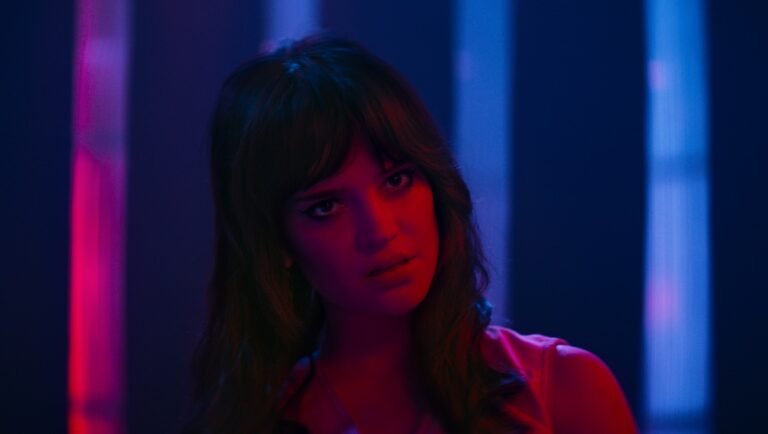 Woman with dark hair looks pensive under red and blue neon lighting.