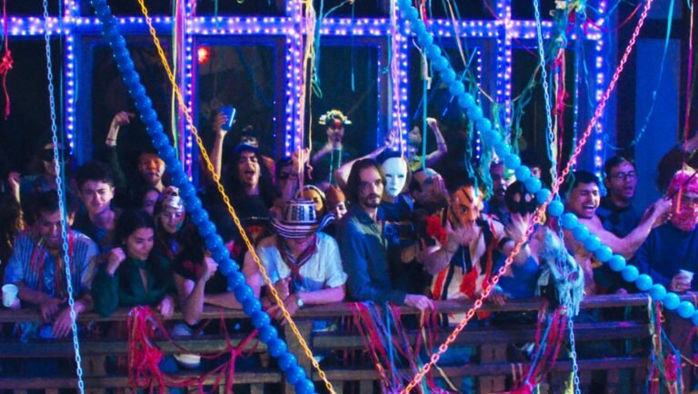 Festive gathering shows people wearing masks and party decorations under bright blue lights.