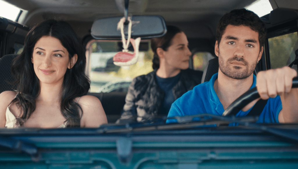 A man drives a car with a smiling woman in the passenger seat and a woman sitting in the back.