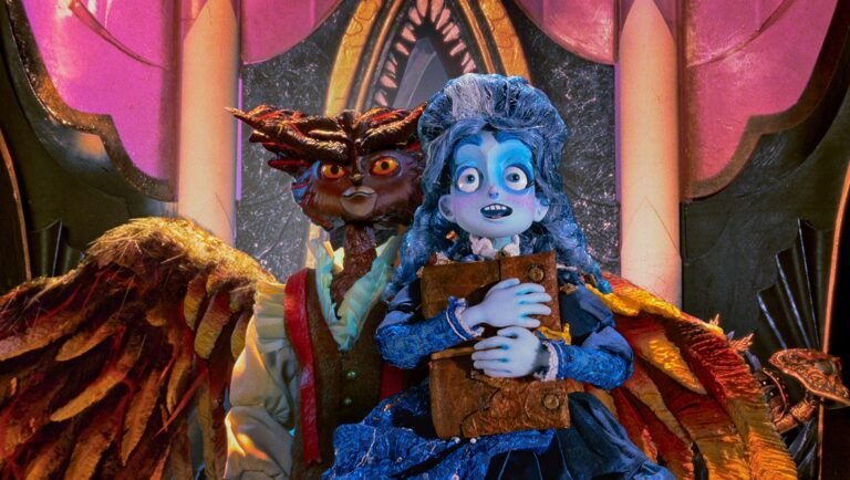 Frankelda and her winged companion holding a large book in a gothic, purple-lit theater set.