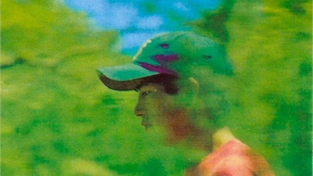 Profile view of a person wearing a green baseball cap against a vibrant, out-of-focus green forest background.