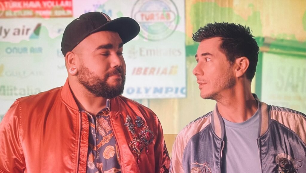 Two men in bomber jackets stand before a backdrop featuring airline logos including Emirates and Iberia.