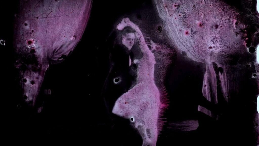 Silhouetted figure dances against a pitch-black background with swirling, eroded lavender-toned film textures.