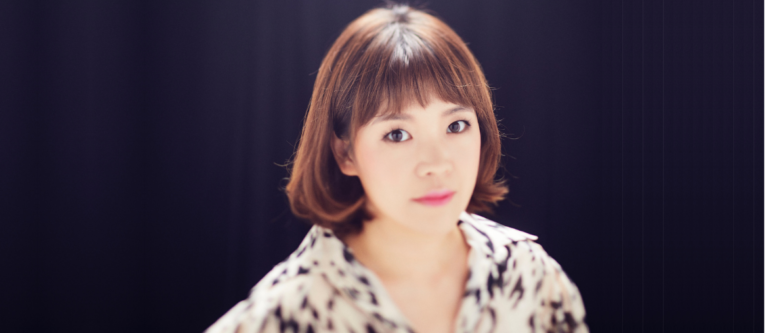 Xue Ma with shoulder-length brown hair and bangs wearing a patterned top against a dark background.