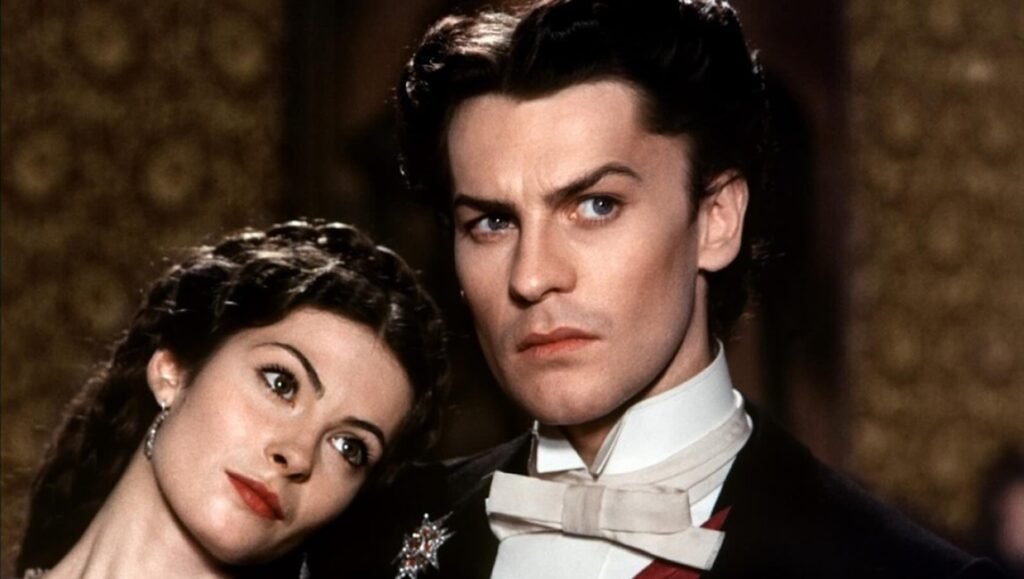 Close-up of a man in formal tuxedo attire looking intensely forward while a woman leans her head on his shoulder.