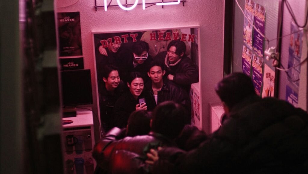 Group of young men taking a mirror selfie in a dimly lit room with pink neon light and Dirty Heaven signage.