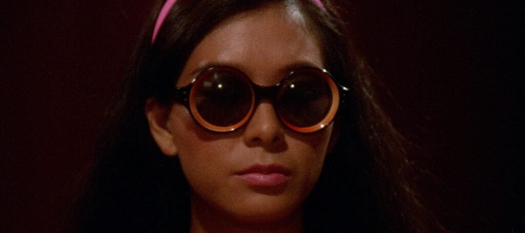 Our Skin and Flesh is Our Own: Angie Chen’s My Name Ain’t Suzie Young woman with long dark hair and a pink headband wearing large, round, orange-rimmed sunglasses.