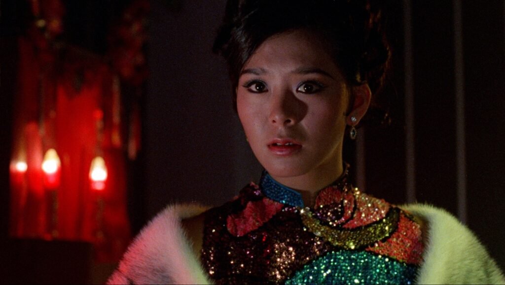 Young woman with an expressive, startled gaze wearing a sequined top and white fur stole in a dimly lit room.