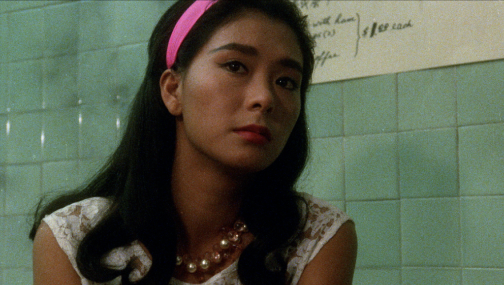 Young woman with a pink headband and pearl necklace looking forward against a green tiled wall.