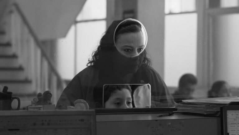 Woman looking through a circular glass window at a service counter with a child appearing in a small rectangular slot.