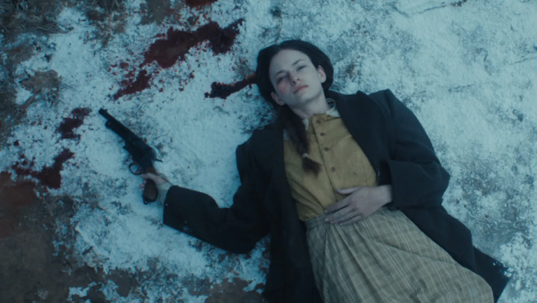 Woman in period clothing lies on snowy ground with a revolver in her hand near a pool of blood.