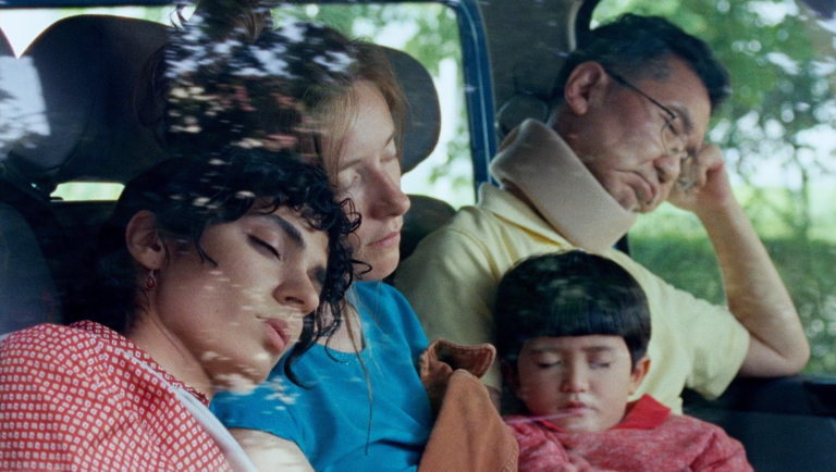 Four diverse people sleep soundly inside a car, including a man wearing a beige neck brace.